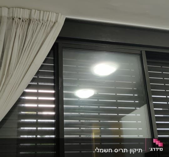 תריסים סגורים על חלון זכוכית עם וילון לבן בצד